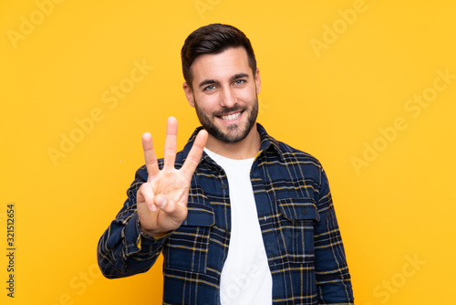 Fotografie Young handsome man with beard over isolated yellow background happy and counting