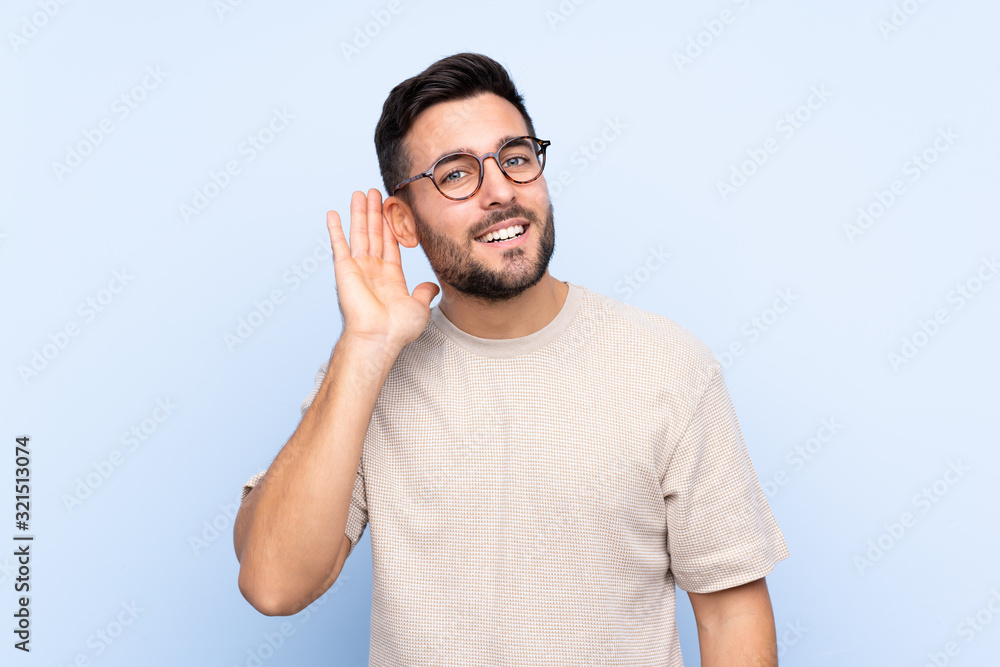 Young handsome man with beard over isolated blue background listening something Young handsome man with beard over isolated blue background listening something