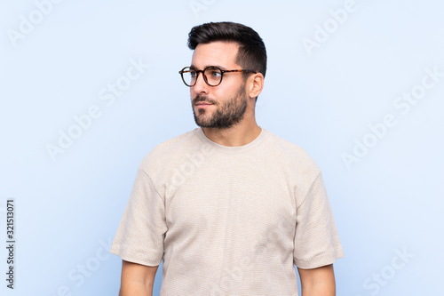 Young handsome man with beard over isolated blue background looking side