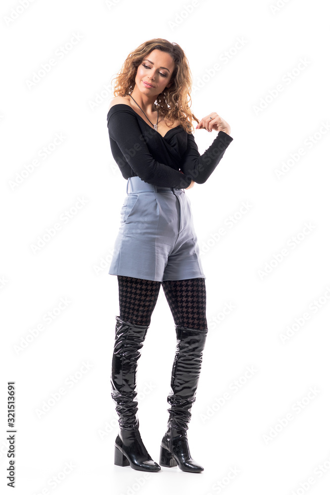 Thoughtful smiling fashionable young woman touching curly hair looking down over shoulder. Full body length isolated on white background. Thoughtful smiling fashionable young woman touching curly hair looking down over shoulder. Full body length isolated on white background.