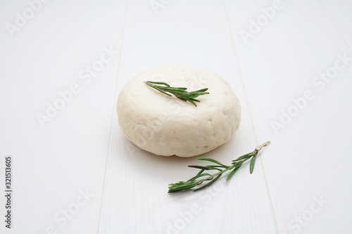 White round cheese, on a wooden white background, garnished with rosemary. The concept of cheeses. photo