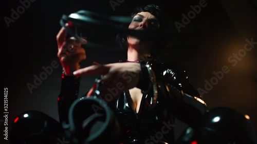 Dominatrix squatting with handcuffs in his hands and a whip.