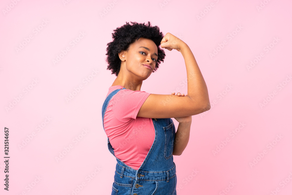 African american woman with overalls over isolated pink background making strong gesture African american woman with overalls over isolated pink background making strong gesture