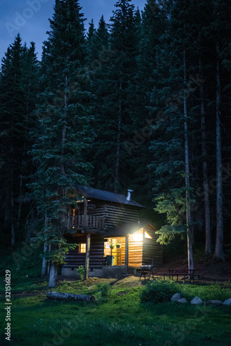 Cabin in woods at night with front porch light on
