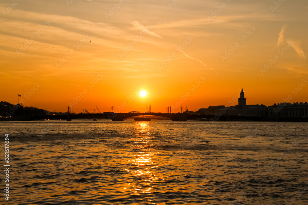 Cityscape of Saint Petersbrug city in Russia during sunset. View of the setting sun over the Neva River and the silhouettes of buildings and a bridge. Theme of travel in Russia.