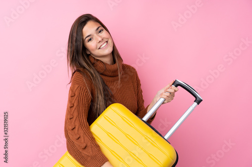 Teenager girl over isolated pink background in vacation with travel suitcase photo