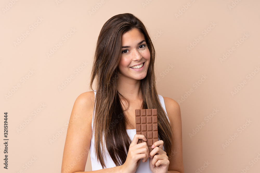Fototapeta premium Teenager girl over isolated background taking a chocolate tablet and happy