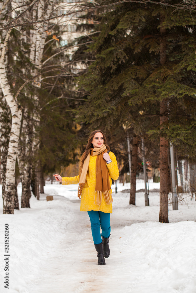 Young beautiful woman in yellow coat walking winter park