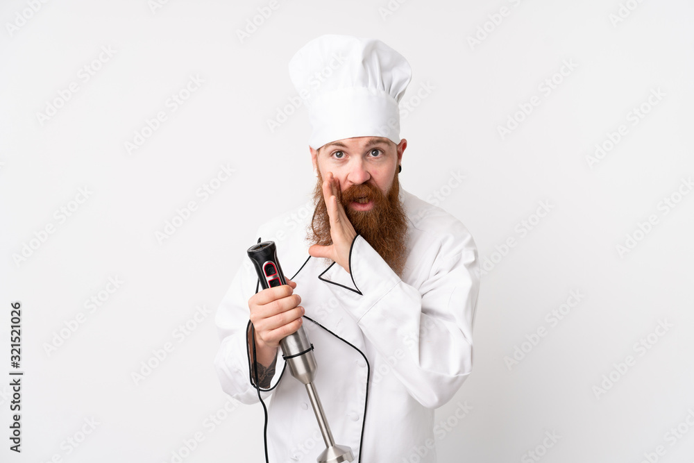 Redhead man using hand blender over isolated white background whispering something Redhead man using hand blender over isolated white background whispering something