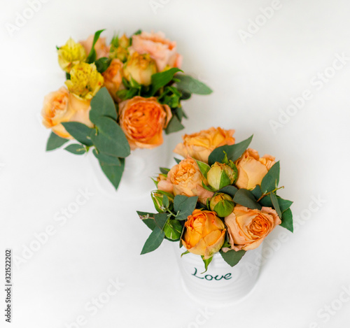Fototapeta Naklejka Na Ścianę i Meble -  flower arrangement of orange roses and green leaves of eucalyptus in a vintage pot on a white background. partial blur. concept of holiday, love, compliment