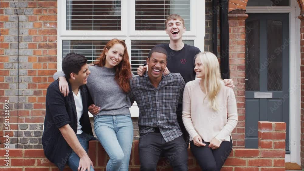 Outdoor Portrait Of Student Friends Sitting On Wall Outside Shared House Together