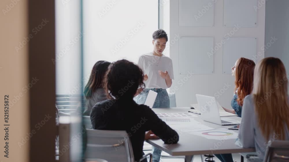 View Through Door As Female Boss Gives Presentation To Team Of Businesswomen Meeting Around Table 