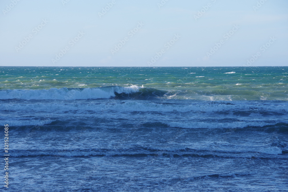 Panoramic view of the rough water surface and waves near the beach of an ocean bay on a windy blue sky winter day
