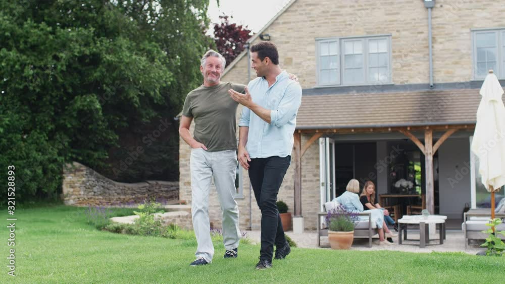 Senior Father With Adult Son Walking And Talking In Garden Together Senior Father With Adult Son Walking And Talking In Garden Together