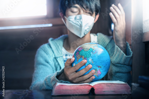 Close up hands of christian young man in mask, holding the globe and praying for peaple in the world, stop Disease Virus and War, christian concept. photo