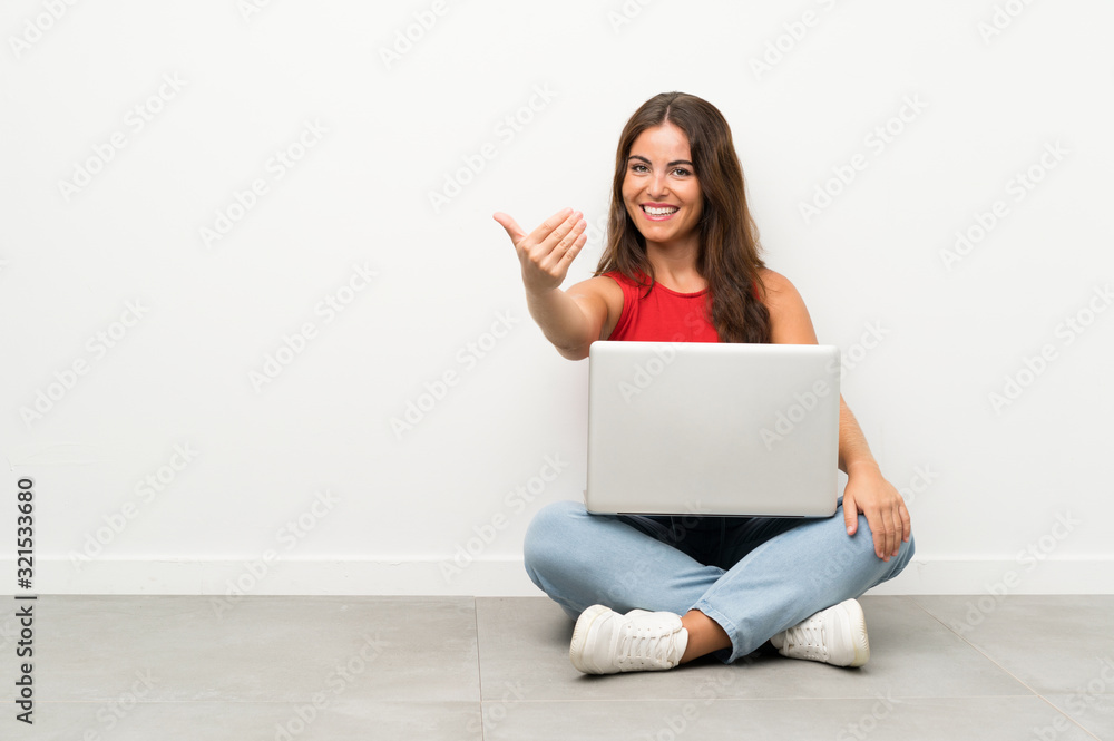 Young woman with a laptop sitting on the floor inviting to come Young woman with a laptop sitting on the floor inviting to come