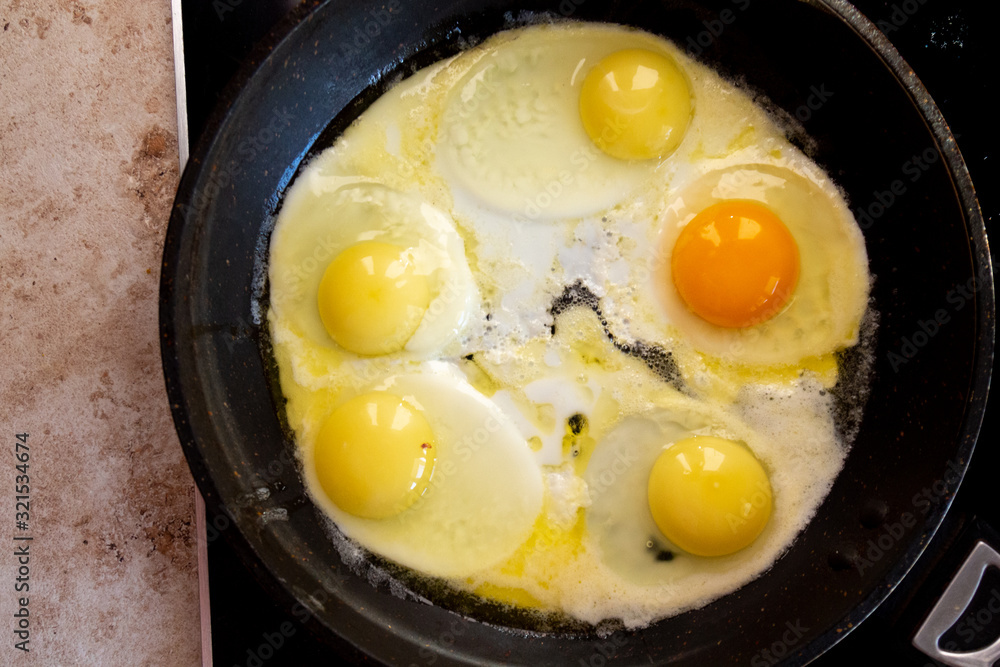 Bright orange egg yolk in a frying pan on a black skillet while preparing a family breakfast. Bright orange egg yolk in a frying pan on a black skillet while preparing a family breakfast.