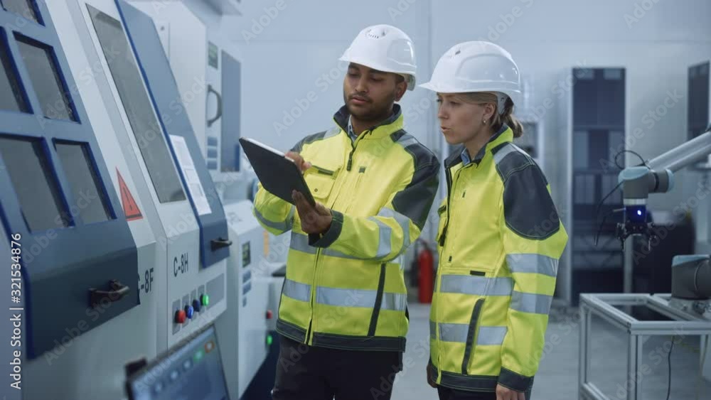 Chief Engineer and Project Manager Wearing Safety Vests and Hard Hats, Use Digital Tablet Computer in Modern Factory, Talking, Optimizing CNC Machinery, Programming Machine for Increasing Efficiency Chief Engineer and Project Manager Wearing Safety Vests and Hard Hats, Use Digital Tablet Computer in Modern Factory, Talking, Optimizing CNC Machinery, Programming Machine for Increasing Efficiency