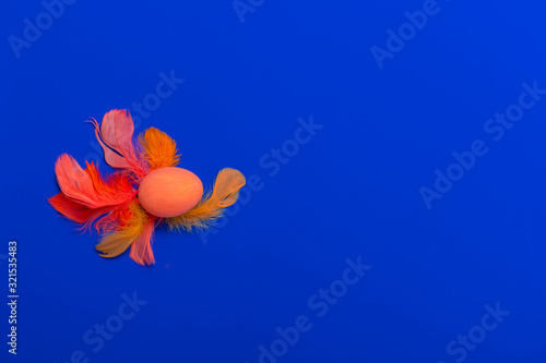 Happy Easter flat lay of orange, red feathers and hand-painted eggs on a blue background. Easter minimal creative greeting card. Copy space.