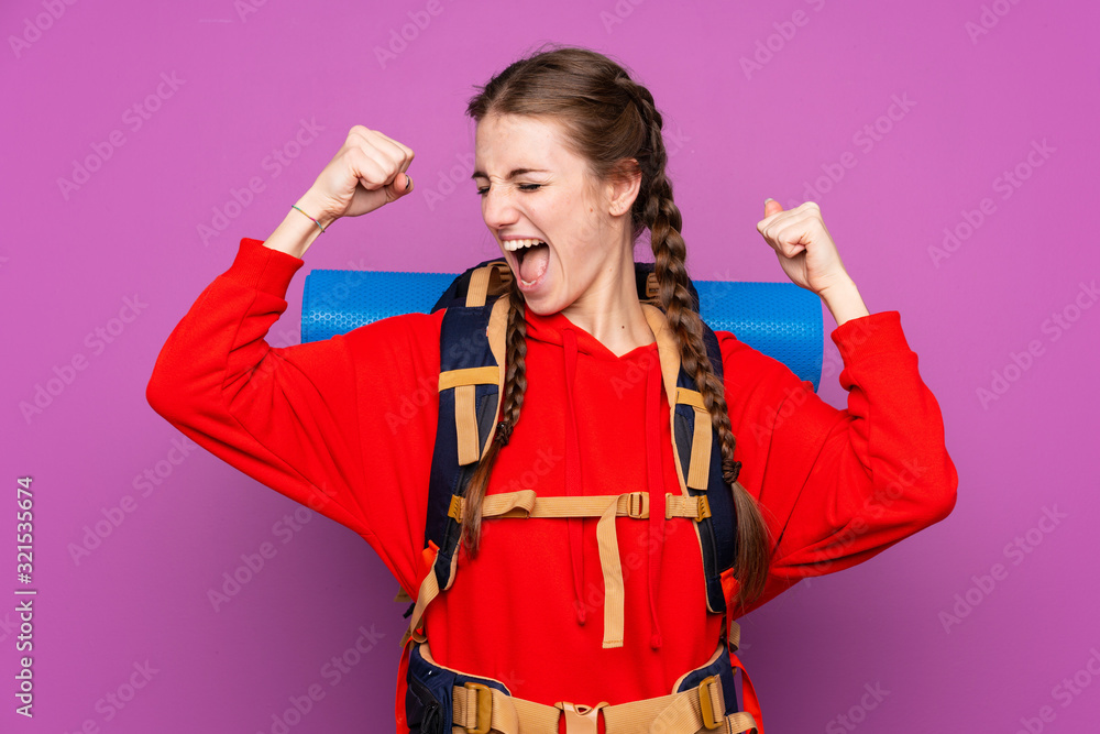 Young mountaineer girl with a big backpack over isolated purple background celebrating a victory Young mountaineer girl with a big backpack over isolated purple background celebrating a victory