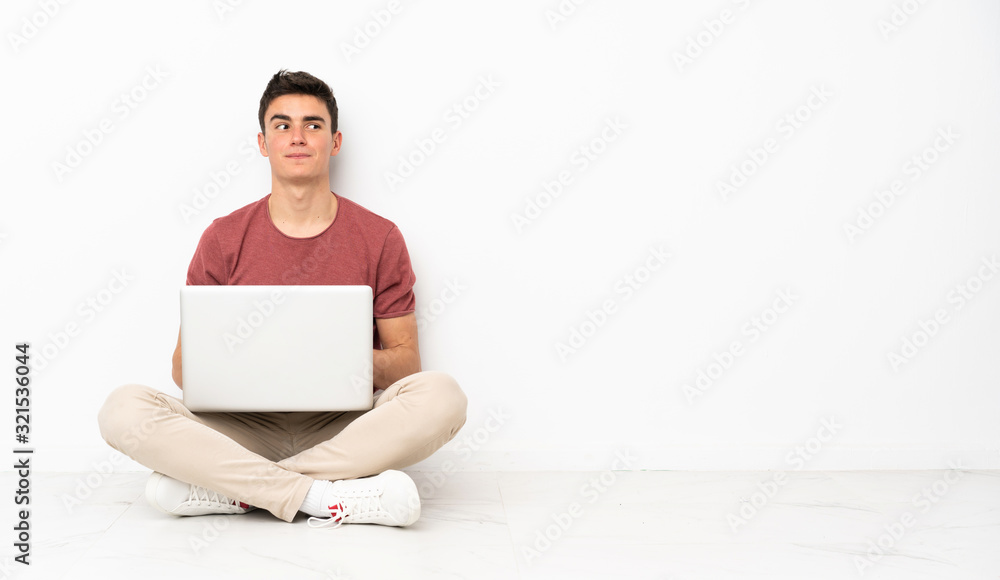 Teenager man sitting on the flor with his laptop making doubts gesture looking side Teenager man sitting on the flor with his laptop making doubts gesture looking side