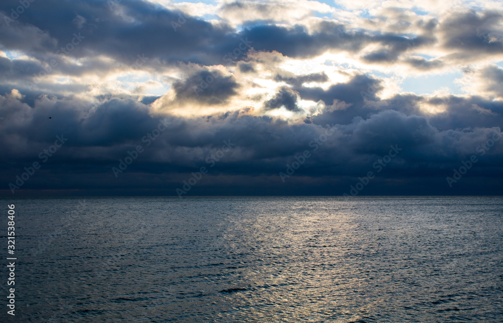 Fototapeta premium blue dark stormy clouds above the sea, the sunlight breaks through the clouds