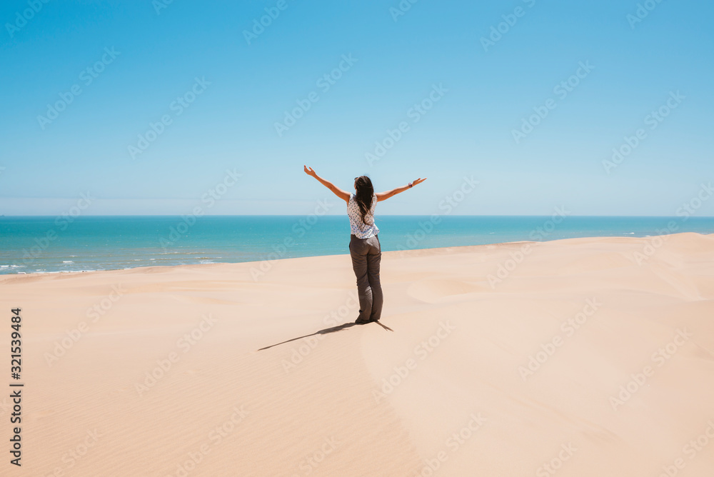 Namibia, Namib desert, Swakopmund, woman in the desert with the sea in the background Namibia, Namib desert, Swakopmund, woman in the desert with the sea in the background