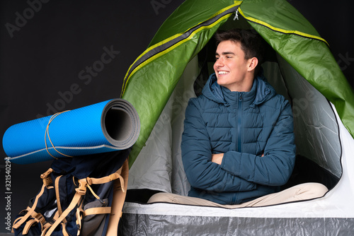 Teenager caucasian man inside a camping green tent isolated on black background in lateral position