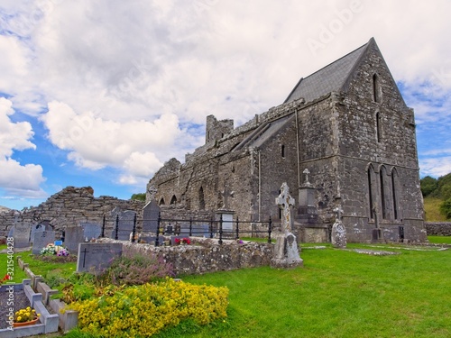 A view on the backside of Corcomroe Abbey and graves of the historic cemetary in front of a blue sky with clouds
