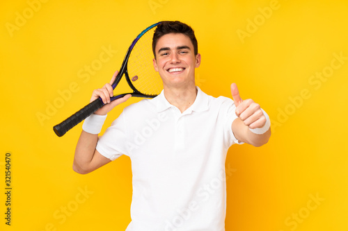 Handsome teenager tennis player man isolated on yellow background playing tennis and with thumb up © luismolinero
