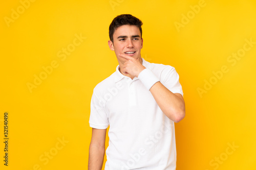 Handsome teenager tennis player man isolated on yellow background playing tennis and thinking