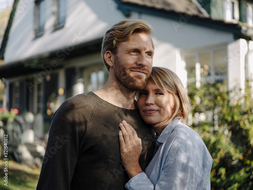 Portrait of smiling couple standing in front of their home photo