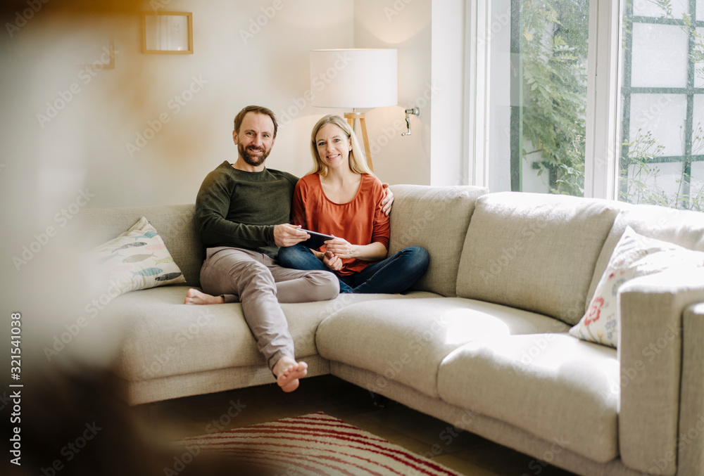 Couple sitting at home on couch, using digital tablet Couple sitting at home on couch, using digital tablet