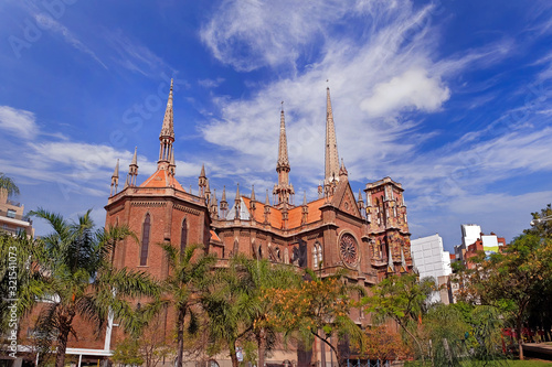 Capuchins Church in Cordoba, Argentina, surrounded by green vegetation, against a blue sky covered by white clouds.
