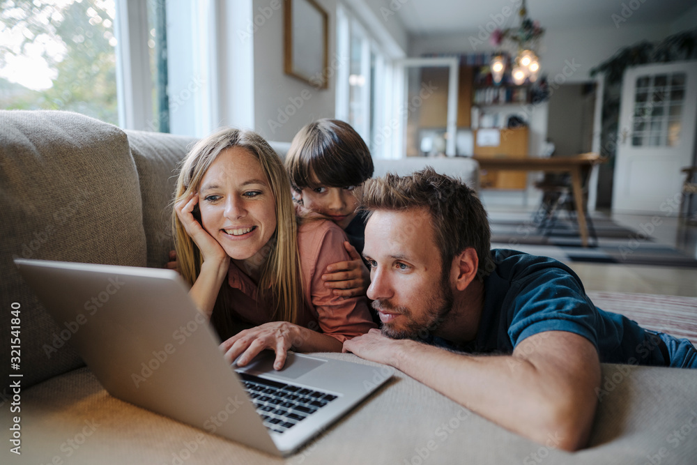© Westend61 - Happy family lying on couch, using laptop