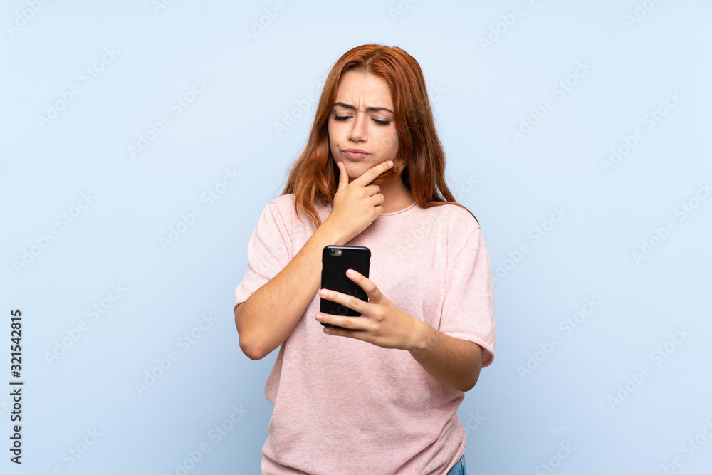 Teenager redhead girl over isolated blue background thinking and sending a message