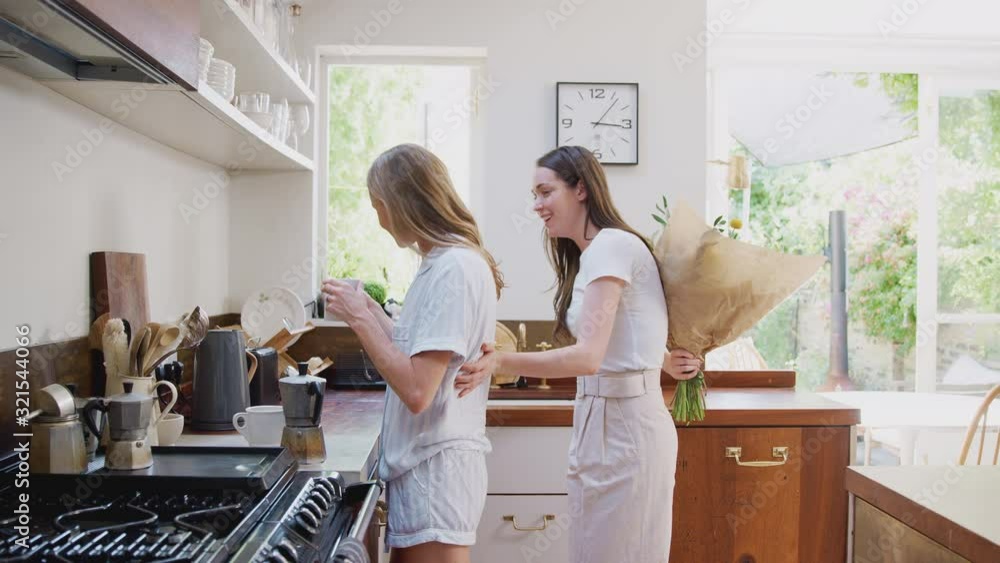 Woman Giving Gay Partner Bunch Of Flowers In Kitchen At Home Woman Giving Gay Partner Bunch Of Flowers In Kitchen At Home