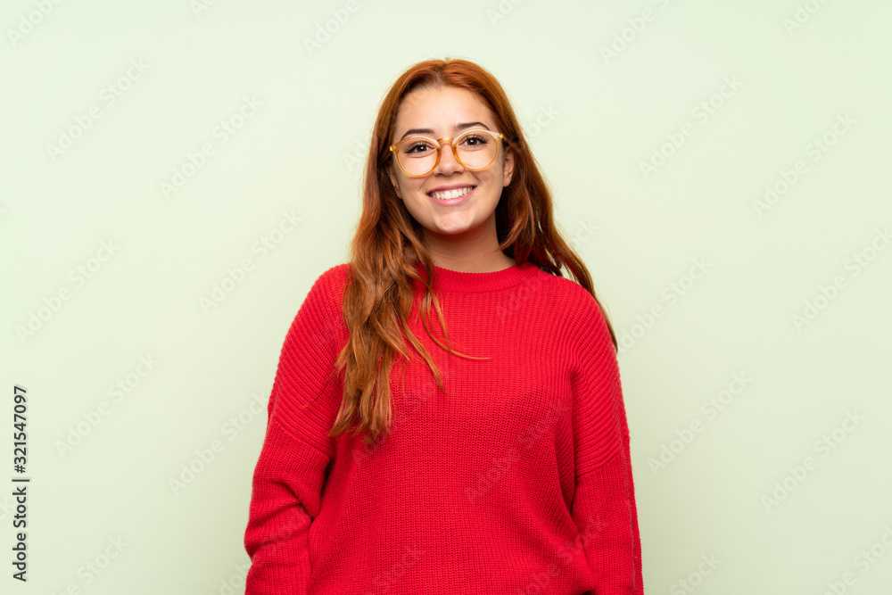 Fototapeta premium Teenager redhead girl with sweater over isolated green background with glasses