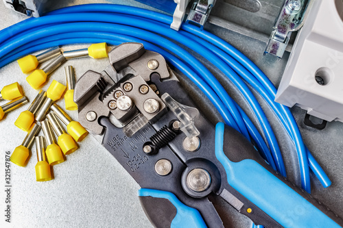 Top view of lying on metal mounting plate wire stripper and blue stranded wire with unused yellow cord end insulated ferrules