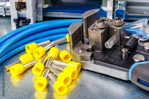 Equipment for wiring close-up. Unused yellow cord end insulated ferrules with wire stripper and blue stranded wire lying on metal mounting plate of electrical panel photo