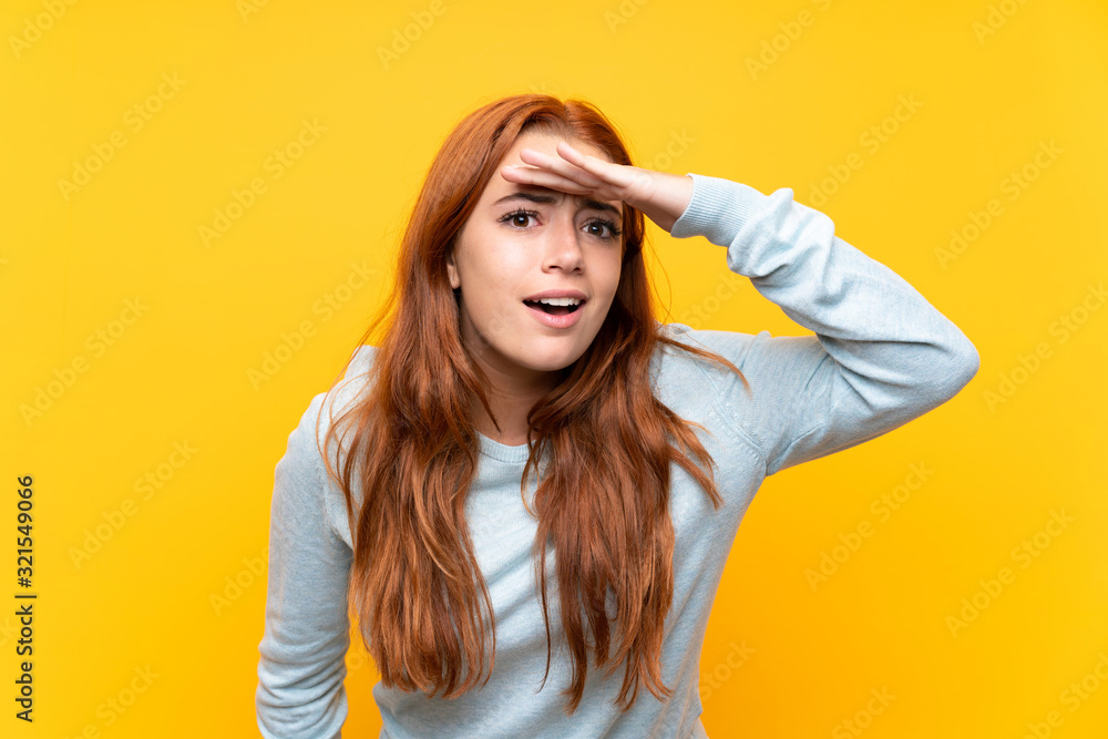 Teenager redhead girl over isolated yellow background looking far away with hand to look something Teenager redhead girl over isolated yellow background looking far away with hand to look something