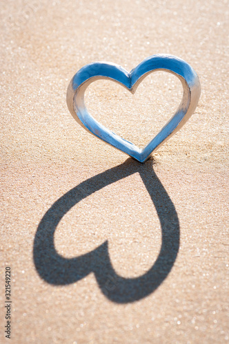 Shiny silver heart standing on the beach casting a shadow on textured sand