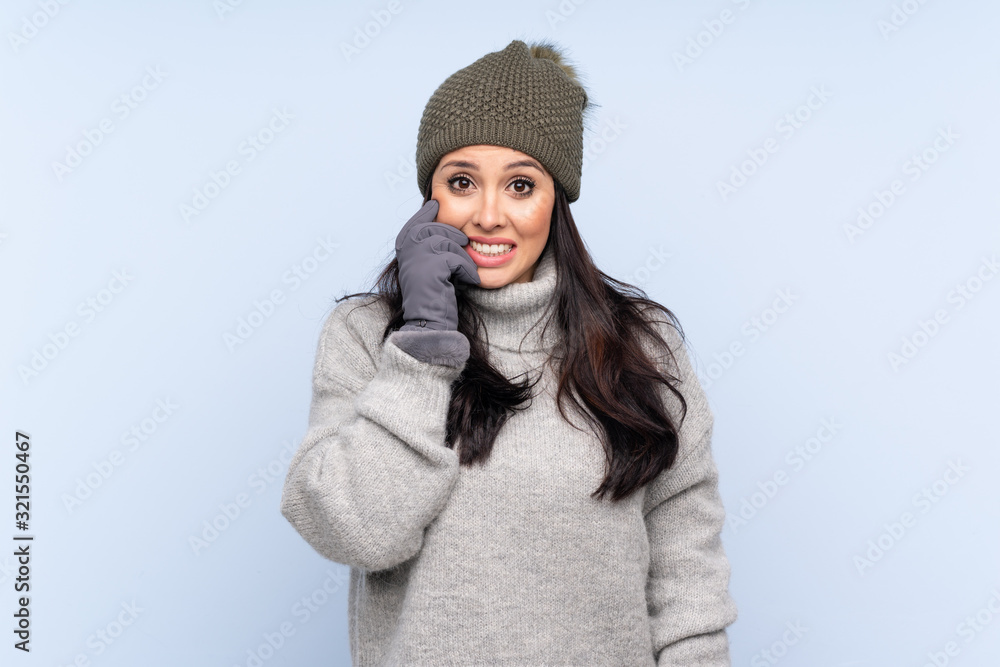 Young Colombian girl with winter hat over isolated blue background nervous and scared Young Colombian girl with winter hat over isolated blue background nervous and scared