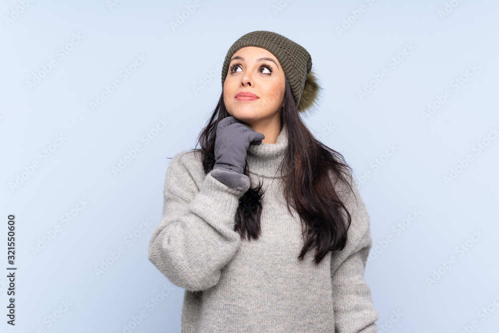 Young Colombian girl with winter hat over isolated blue background thinking an idea
