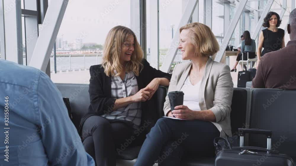 Two Businesswomen Sitting In Airport Departure Talking Together Two Businesswomen Sitting In Airport Departure Talking Together