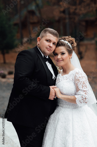 Wedding couple in the forest. Beautiful plus size bride and groom on a walk in autumn park, embrace. White wedding dress. Portrait. Walking newlyweds in nature.