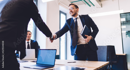 Billede på lærred Smiling confident executive man in eyeglasses holding notebook and shaking hand