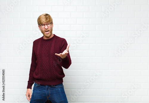 young blonde man looking angry, annoyed and frustrated screaming wtf or what’s wrong with you agaist vintage tiles wall photo