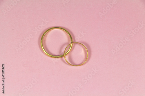 Two wedding rings made in gold on pink background