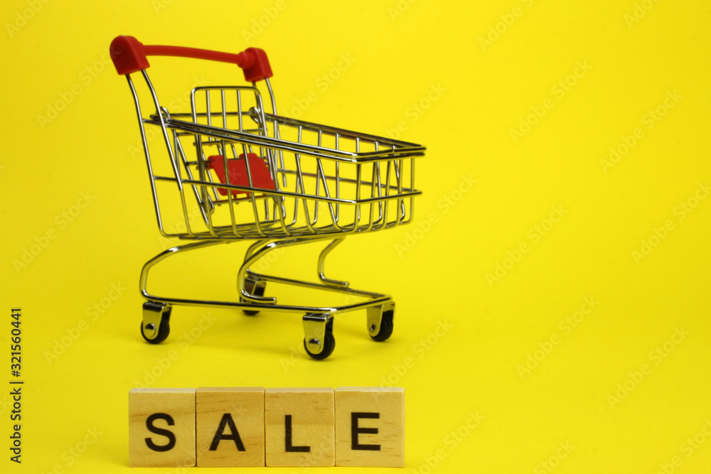 Mini supermarket cart, trolley on a yellow background. Purchases. The Word Sale Mini supermarket cart, trolley on a yellow background. Purchases. The Word Sale